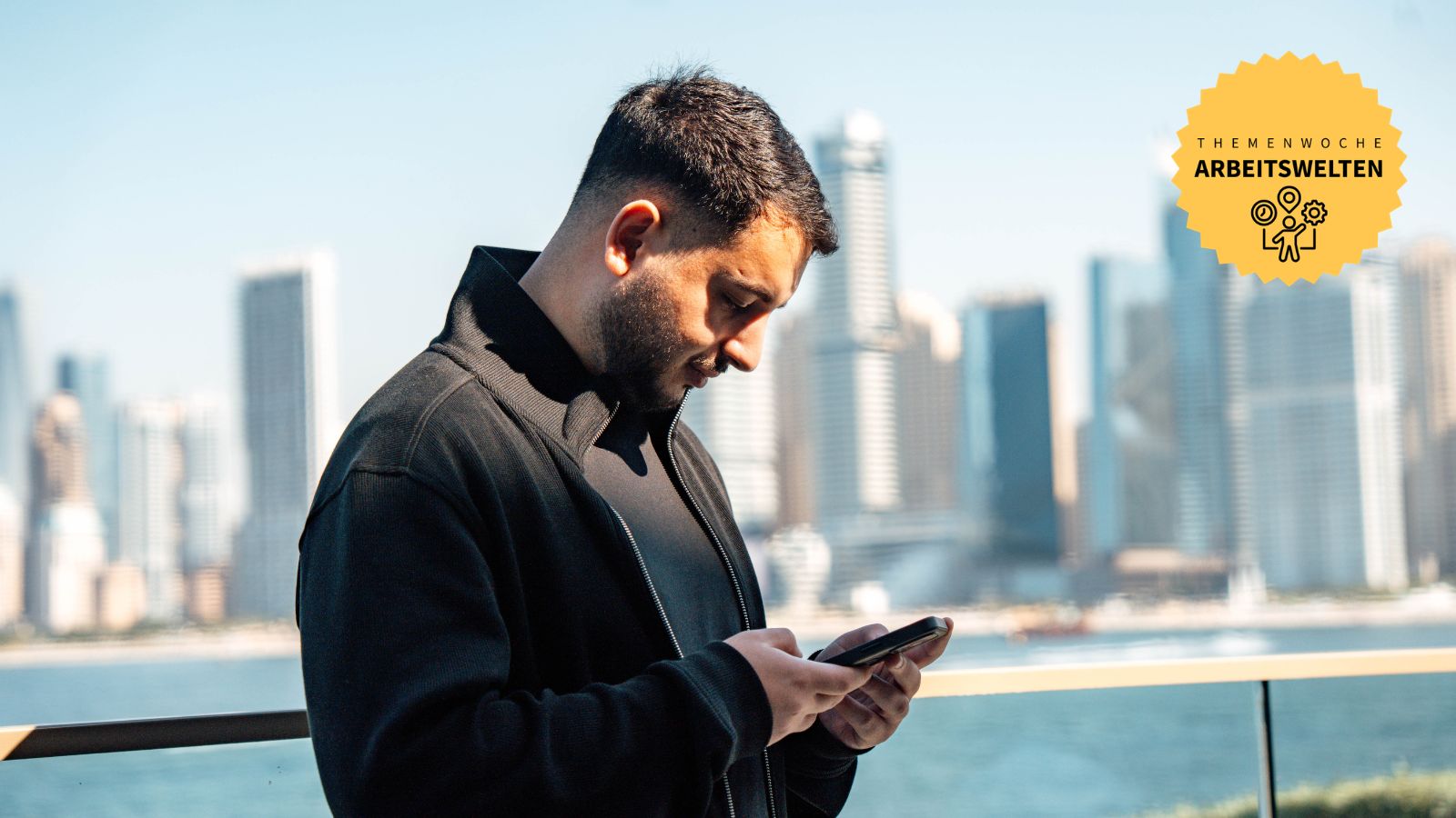 Hakan Ersu vor der Skyline einer Stadt schaut auf sein Smartphone